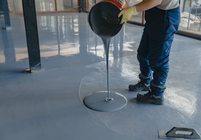 Worker applying industrial floor paint in a large warehouse facility