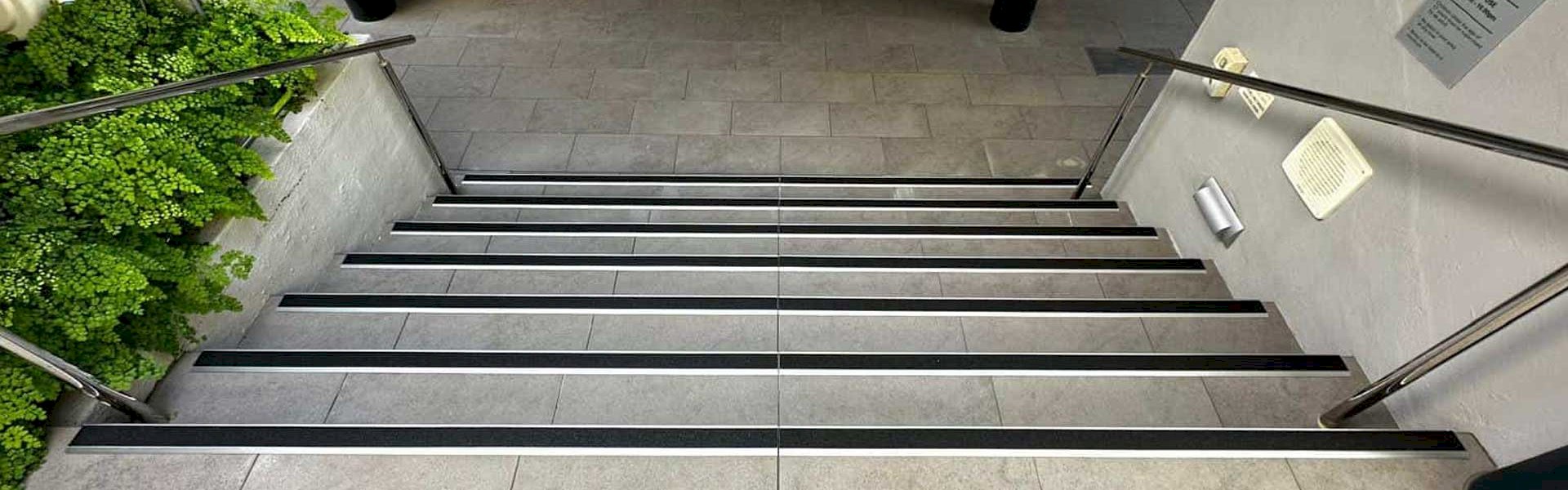 Side-by-side comparison of Aluminator and aluminium stair nosings on high-traffic staircases in an industrial or commercial setting